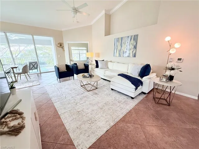 Living room with lofted ceiling, light tile patterned floors, ceiling fan, and crown molding