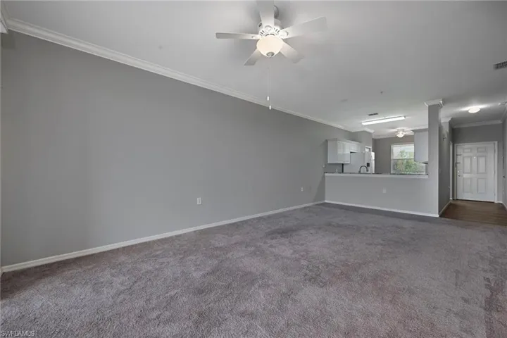 Unfurnished living room with crown molding, ceiling fan, and dark colored carpet