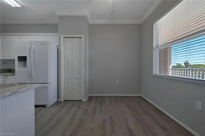 Kitchen with white refrigerator with ice dispenser, white cabinetry, light wood-style flooring, light stone counters, and crown molding