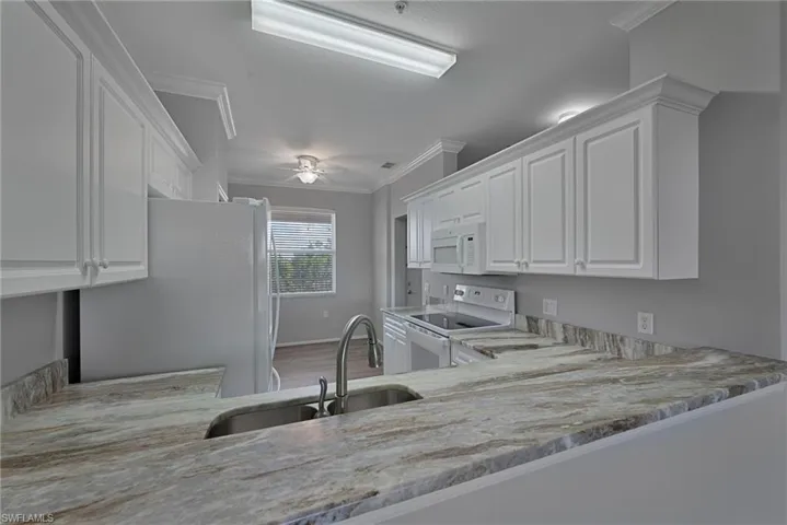 Kitchen with white cabinets, crown molding, white appliances, ceiling fan, and light stone countertops
