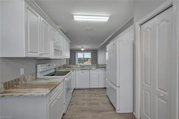 Kitchen with white appliances, white cabinetry, light wood-style floors, and ornamental molding