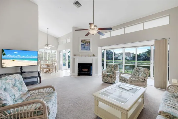 Living area with light colored carpet, ceiling fan, a fireplace with flush hearth, a water view, and vaulted ceiling
