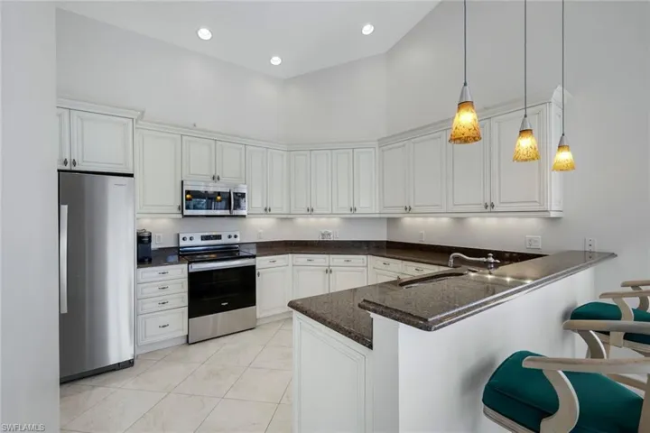 Kitchen featuring stainless steel appliances, a high ceiling, a kitchen bar, a peninsula, and decorative light fixtures