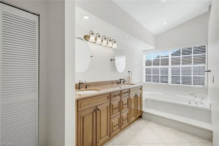 Full bathroom with double vanity, a closet, a garden tub, light tile patterned floors, and lofted ceiling