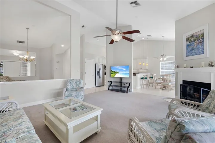 Living room featuring a chandelier, light colored carpet, ceiling fan, a fireplace, and vaulted ceiling