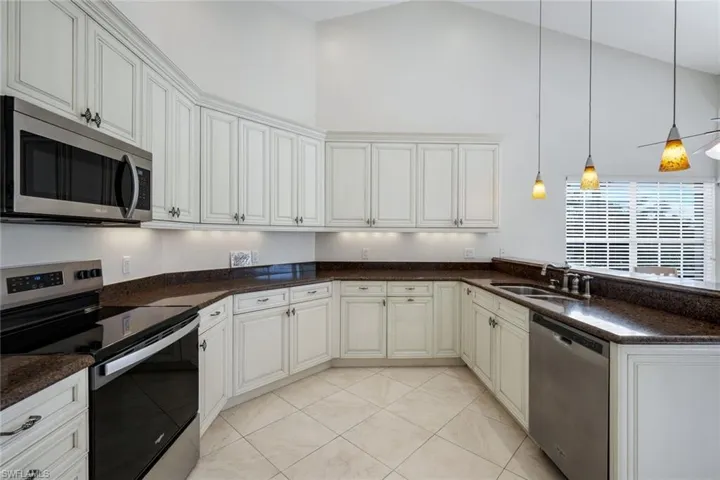 Kitchen featuring stainless steel appliances, dark stone countertops, decorative light fixtures, a peninsula, and white cabinets