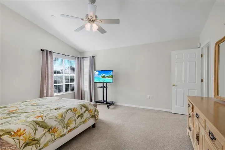 Bedroom with light colored carpet, vaulted ceiling, and ceiling fan