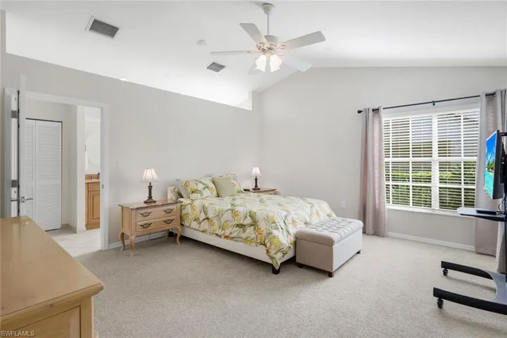 Bedroom featuring light colored carpet, vaulted ceiling, a ceiling fan, and ensuite bath