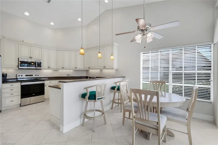Kitchen with stainless steel appliances, hanging light fixtures, a breakfast bar, a peninsula, and dark stone countertops