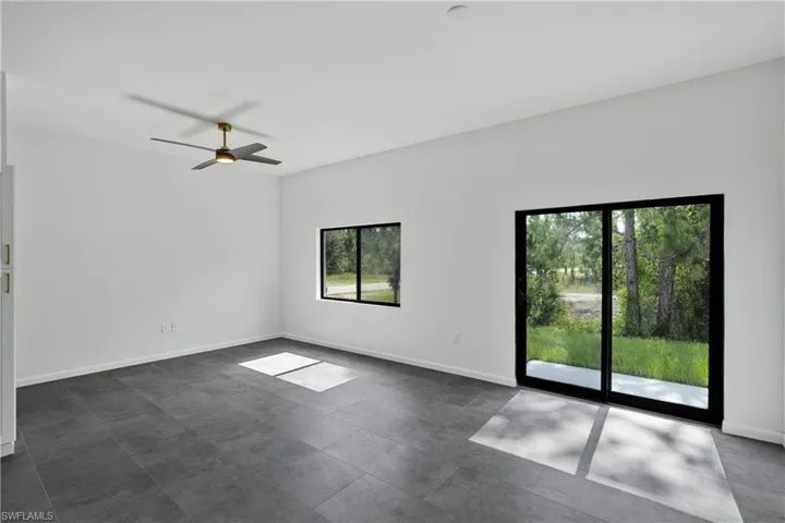 Spacious interior featuring a contemporary ceiling fan with integrated lighting, large format gray floor tiles, and a sliding glass door providing direct outdoor access