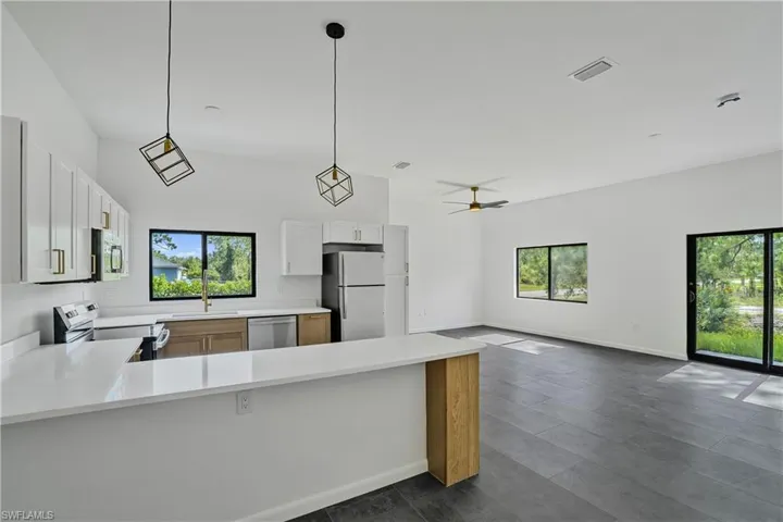 Open-concept living space featuring a modern kitchen with white cabinetry, light wood-finish lower cabinets, stainless steel appliances, and a breakfast bar