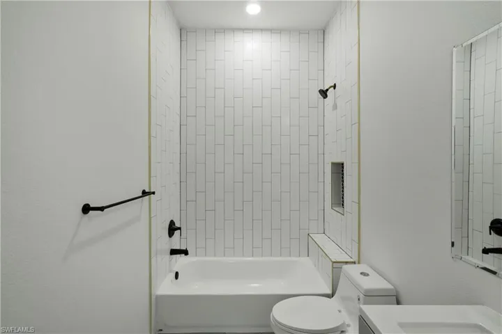Bathroom featuring a white subway tile shower surround with gold accent trim, a built-in shower niche, and a shower bench