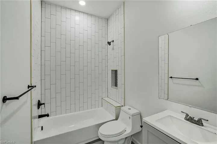 Bathroom featuring a white subway tile shower surround with a built-in niche, white bathtub, and matte black fixtures