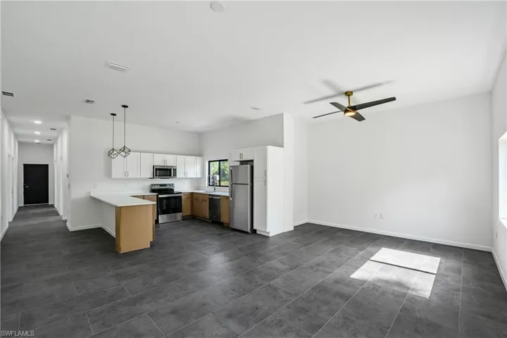 Open-concept living area featuring dark tile flooring, a contemporary ceiling fan, and a kitchen with light wood-finish cabinetry, stainless steel appliances, and a breakfast bar