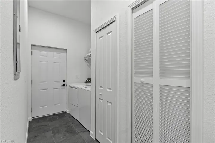 Laundry area featuring dark-toned floor tiling, a white paneled door, louvered bi-fold closet doors, and built-in shelving