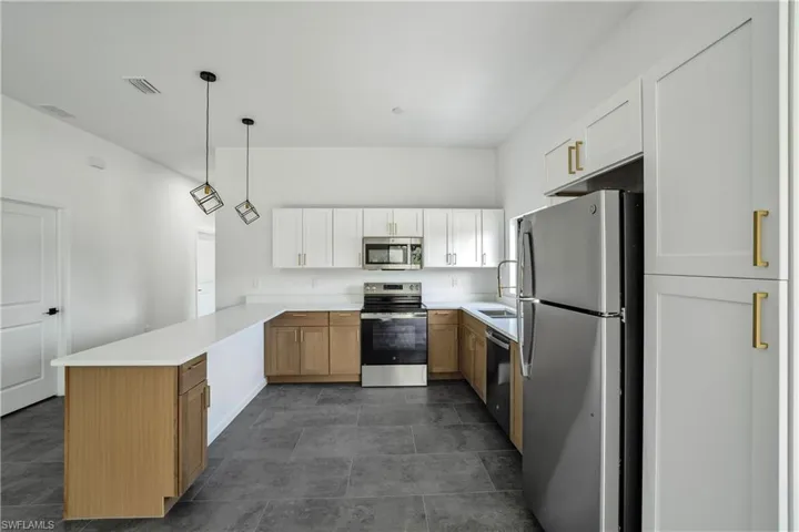 Kitchen featuring a peninsula island, two-tone cabinetry, stainless steel appliances, white countertops, and dark tile flooring