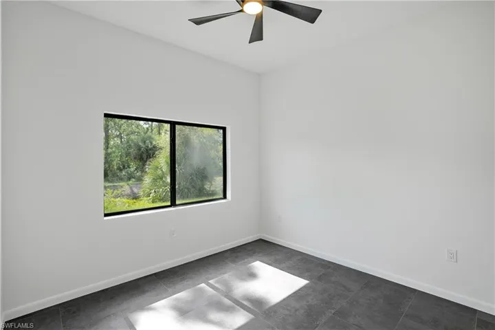 Room featuring a modern ceiling fan, large window with black trim, white walls, and dark gray tile flooring