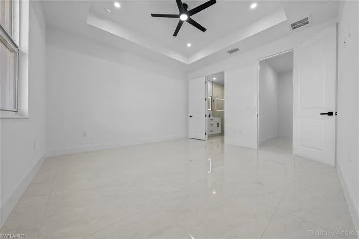 Unfurnished bedroom with ensuite bathroom, recessed lighting, a ceiling fan, and a raised ceiling