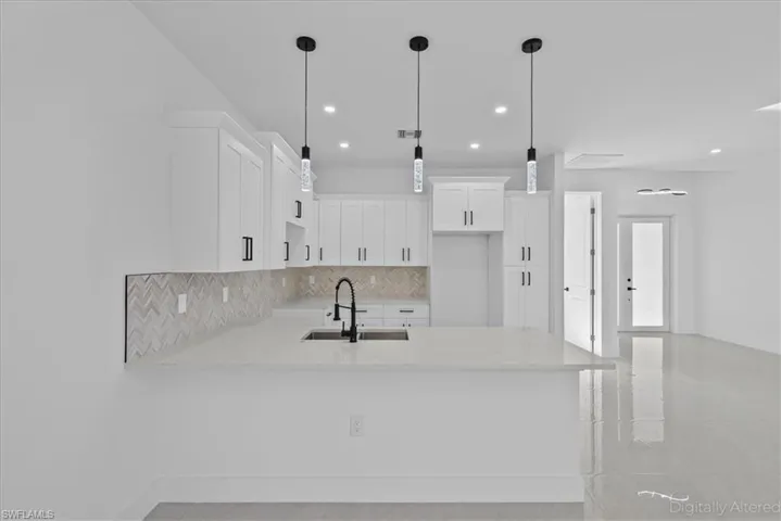 Kitchen featuring decorative backsplash, white cabinetry, light stone counters, and a peninsula
