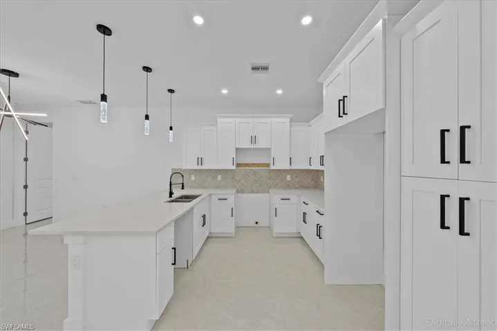 Kitchen featuring white cabinetry, a peninsula, decorative light fixtures, light stone countertops, and decorative backsplash