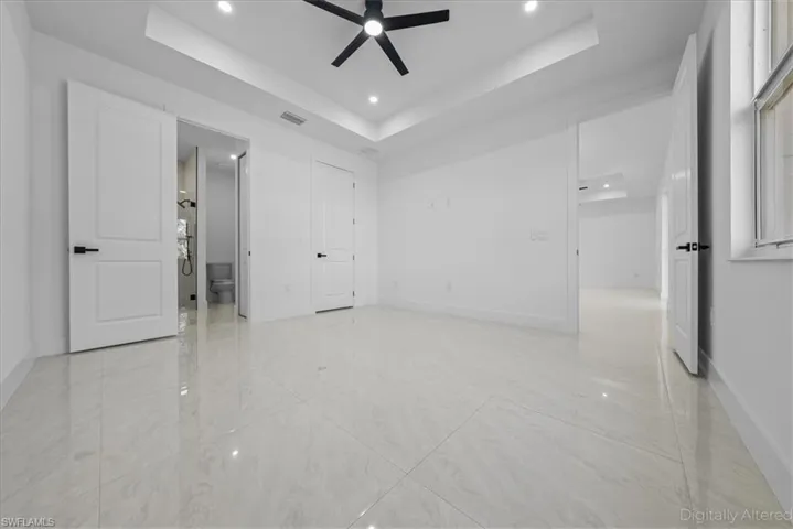 Unfurnished bedroom featuring recessed lighting, a tray ceiling, a ceiling fan, and ensuite bath