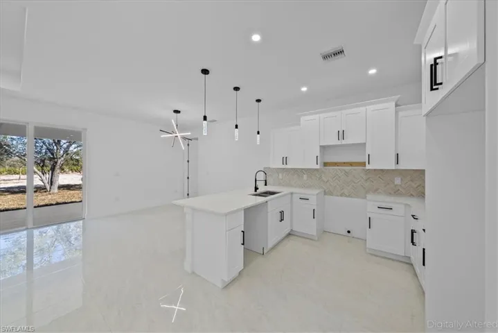 Kitchen featuring white cabinetry, a peninsula, decorative light fixtures, decorative backsplash, and light stone countertops