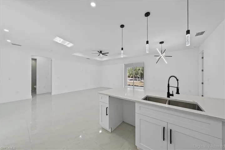 Kitchen with light stone countertops, white cabinets, open floor plan, decorative light fixtures, and ceiling fan