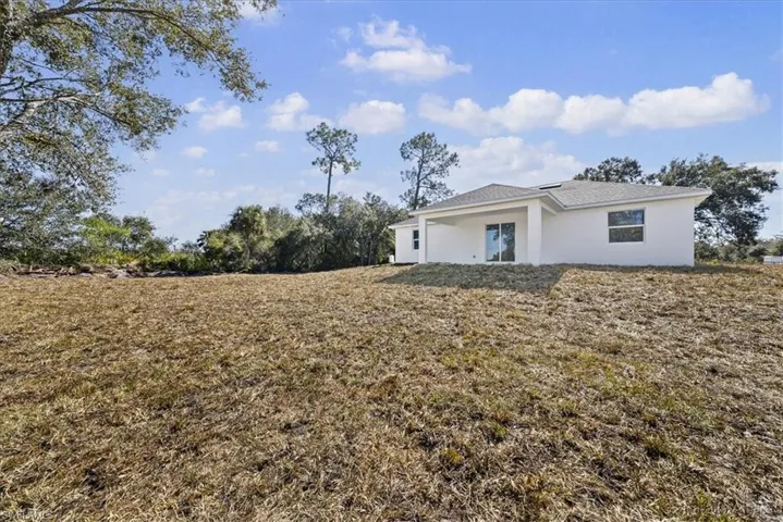 Rear view of house with stucco siding, a lawn, and a patio