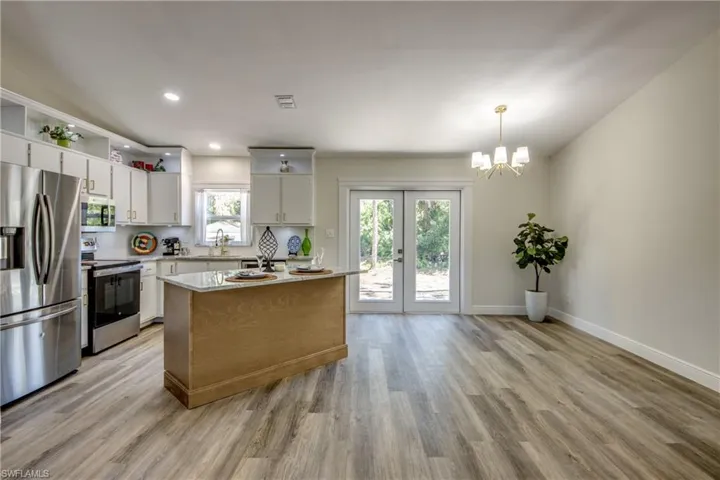 Kitchen with appliances with stainless steel finishes, light wood-type flooring, a sink, a chandelier, and open shelves