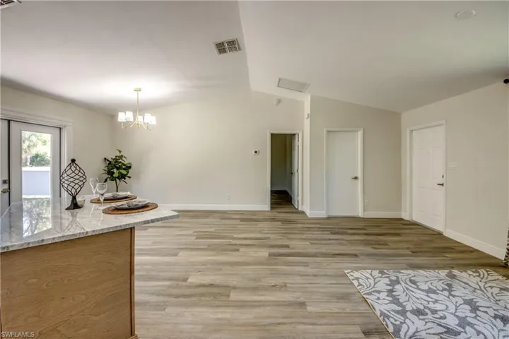 Kitchen with lofted ceiling, light wood finished floors, baseboards, a chandelier, and light stone counters