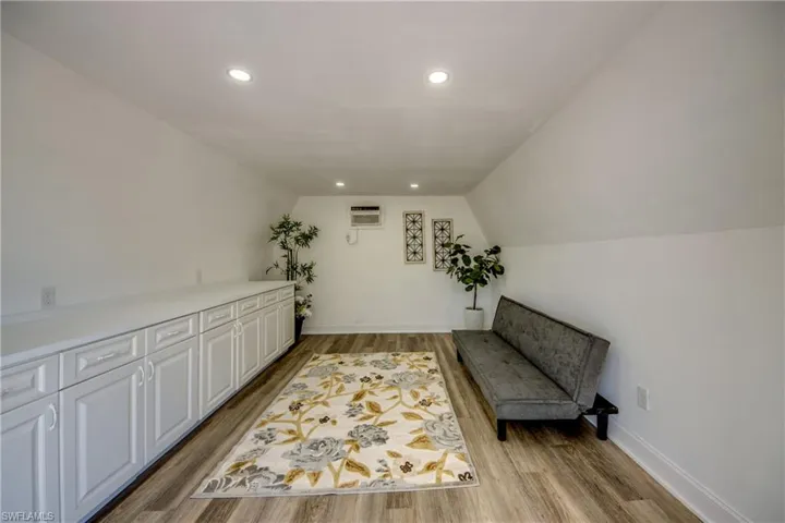 Living area with vaulted ceiling, light wood-type flooring, a wall mounted air conditioner, recessed lighting, and baseboards