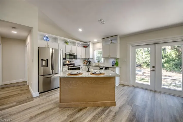 Kitchen with stainless steel appliances, light wood-type flooring, white cabinets, a kitchen island, and lofted ceiling