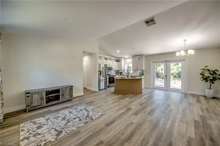Living area with lofted ceiling, a chandelier, light wood-type flooring, french doors, and baseboards