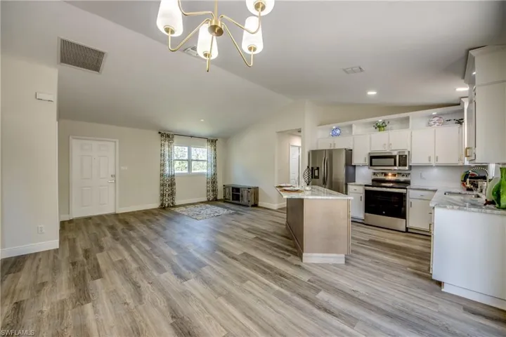 Kitchen with stainless steel appliances, a sink, a chandelier, lofted ceiling, and a kitchen island