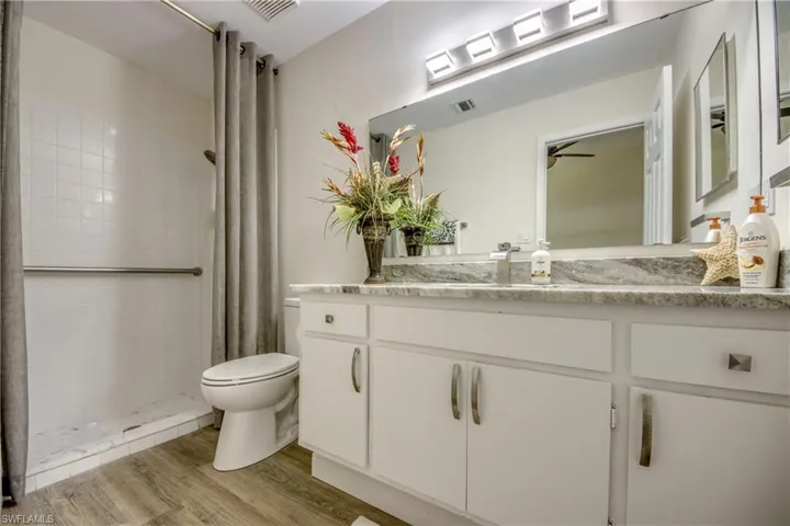 Bathroom with toilet, a tile shower, wood finished floors, vanity, and ceiling fan