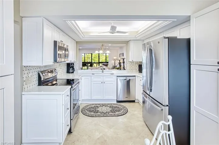 Kitchen featuring a raised ceiling, stainless steel appliances, white cabinets, crown molding, and backsplash