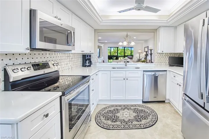 Kitchen with stainless steel appliances, white cabinetry, backsplash, a chandelier, and a raised ceiling