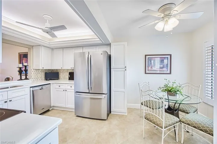 Kitchen featuring a ceiling fan, stainless steel appliances, white cabinetry, a raised ceiling, and ornamental molding