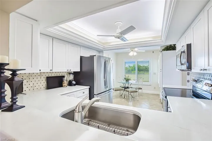 Kitchen featuring stainless steel appliances, decorative backsplash, ornamental molding, light stone counters, and white cabinetry
