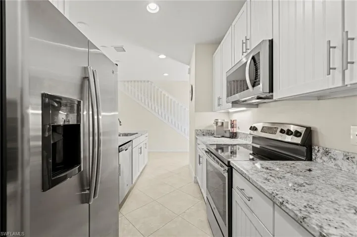 Kitchen featuring light tile patterned floors, white cabinets, light stone countertops, stainless steel appliances, and recessed lighting
