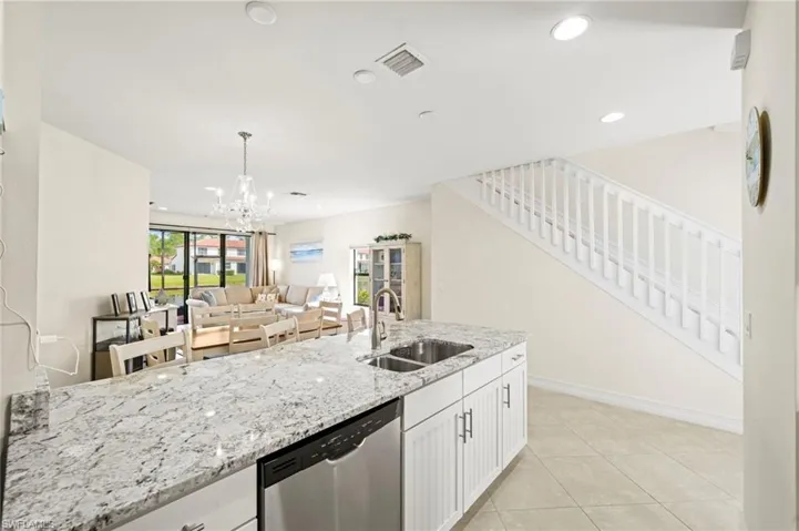 Kitchen with visible vents, light stone countertops, stainless steel dishwasher, white cabinetry, and a sink