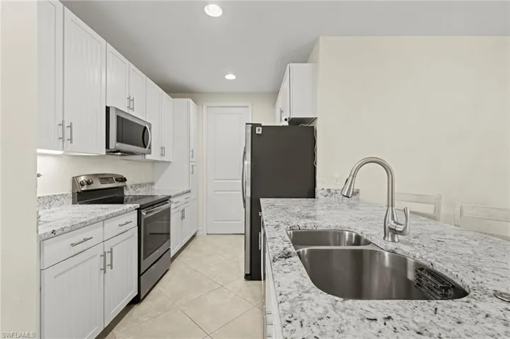 Kitchen featuring light stone counters, light tile patterned floors, stainless steel appliances, white cabinets, and a sink