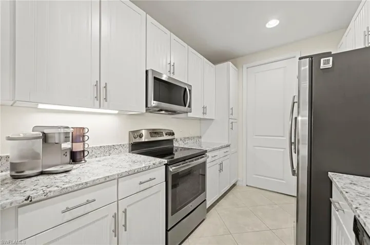Kitchen with stainless steel appliances, white cabinets, light stone counters, and light tile patterned floors