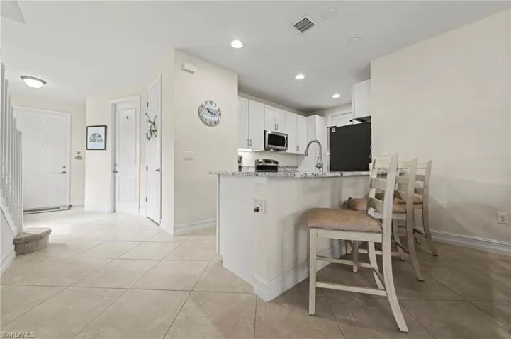 Kitchen with light tile patterned floors, stainless steel microwave, visible vents, a peninsula, and fridge