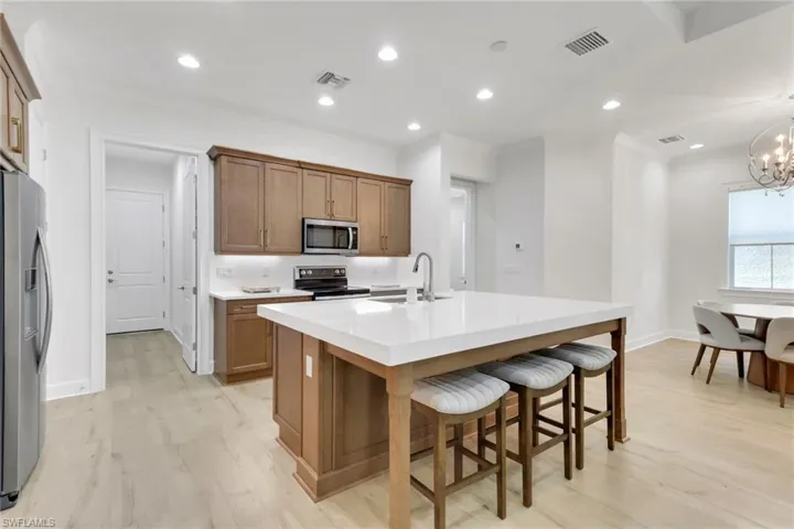 Kitchen featuring brown cabinetry, appliances with stainless steel finishes, light wood-style flooring, a kitchen breakfast bar, and recessed lighting
