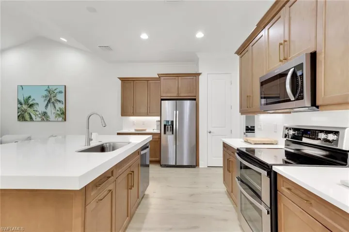 Kitchen with stainless steel appliances, recessed lighting, light wood-style flooring, a kitchen island with sink, and light stone countertops