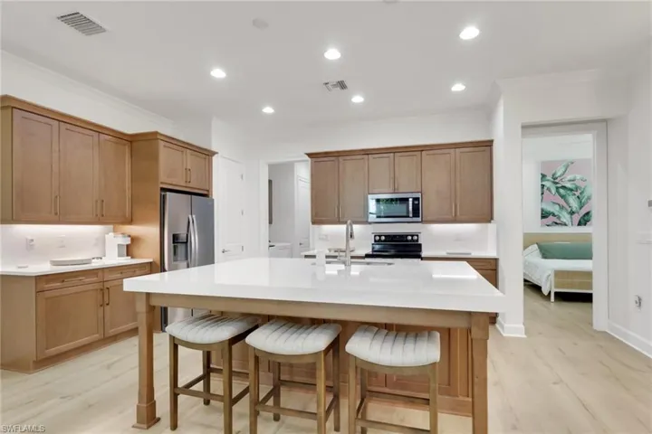 Kitchen with light wood-style flooring, recessed lighting, a kitchen bar, a kitchen island with sink, and ornamental molding