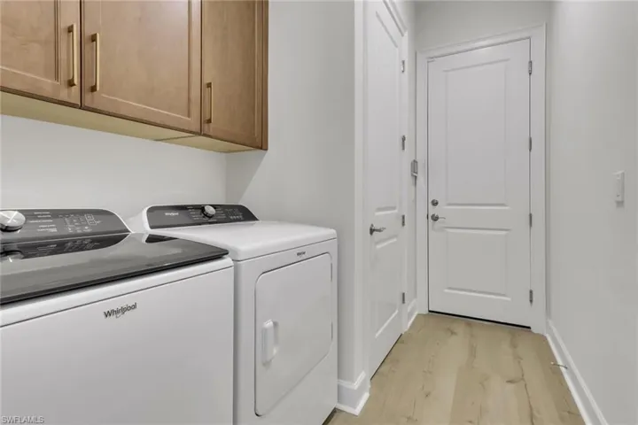 Laundry room featuring light wood-type flooring, cabinet space, and washing machine and clothes dryer