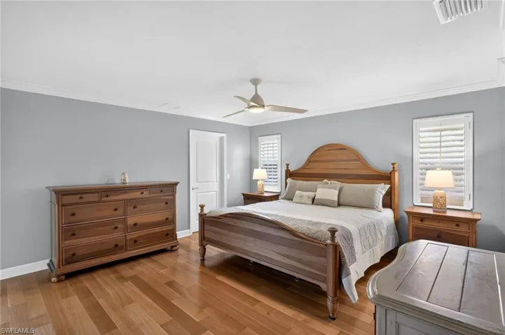 Spacious room featuring wood-finish flooring, white crown molding, two windows with white plantation shutters, and a ceiling fan with integrated lighting