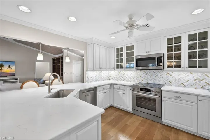 Modern kitchen featuring white cabinetry, stainless steel appliances, light-toned countertops, a herringbone tile backsplash, and wood-finish flooring